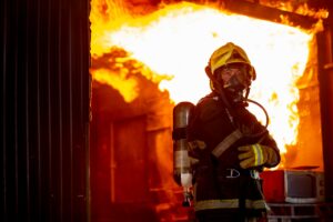 Fire on wall and ceiling in the kitchen behind firefighter man with protective and safety